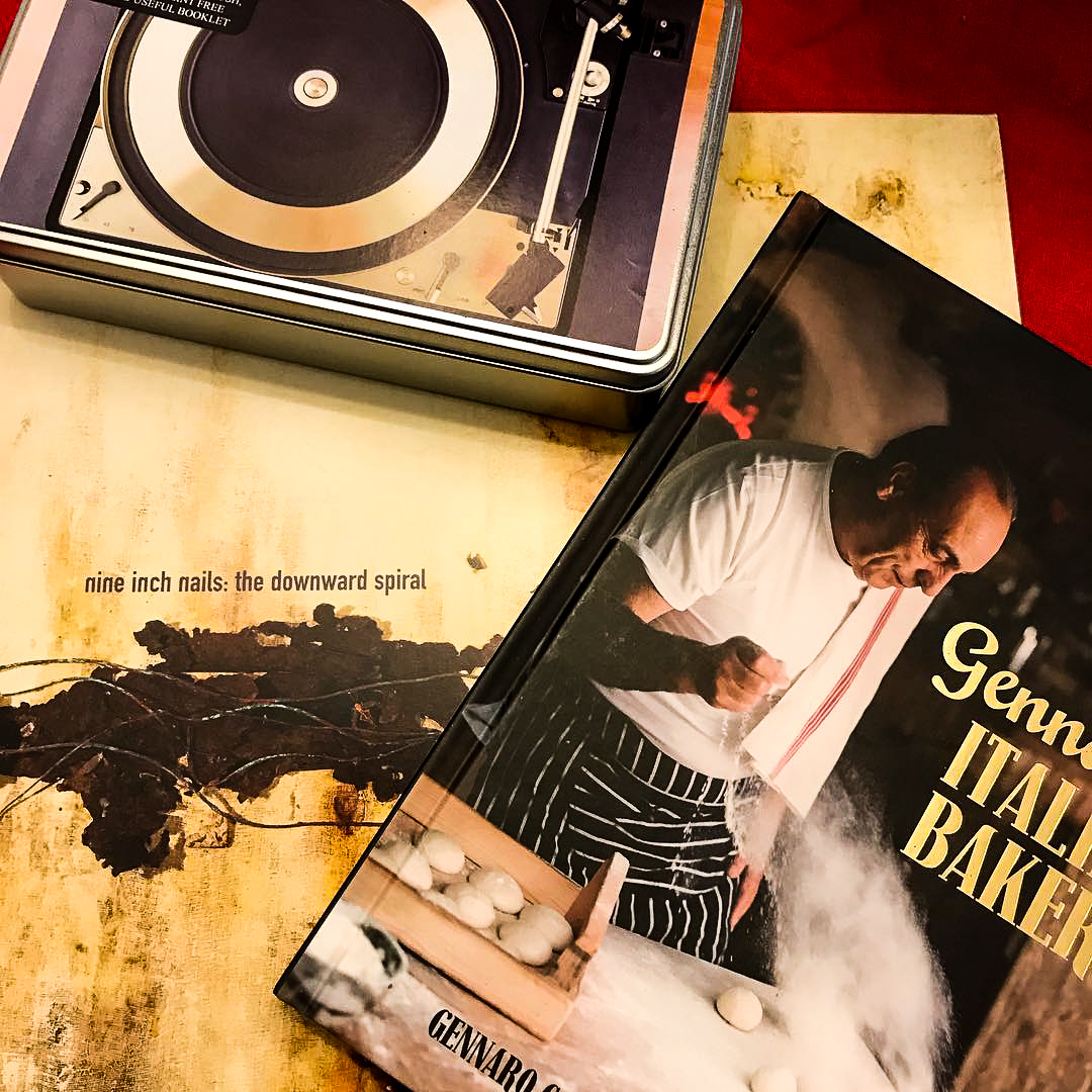A picture of the vinyl of The Downward Spiral by Nine Inch Nails, sat on top of it is the book Gennaro’s Italian Bakery and a record cleaning kit.  